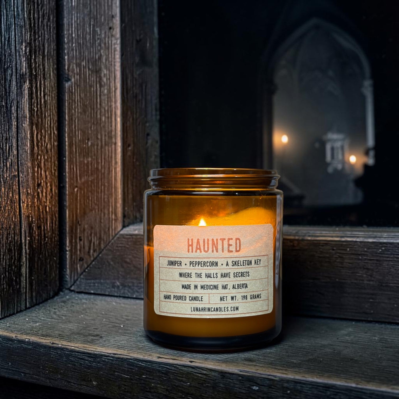Amber glass Haunted candle on a dark wood-paneled windowsill beside an antique skeleton key, faint candlelight glowing around a corner in the shadows