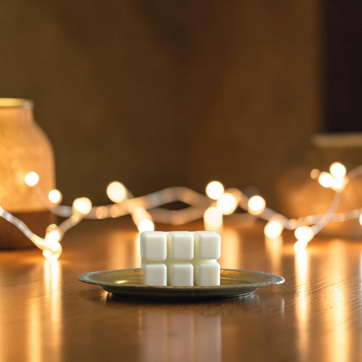 Wax melt on a wood table with trailing greenery and glowing warm white fairy lights in a cozy, softly lit background.